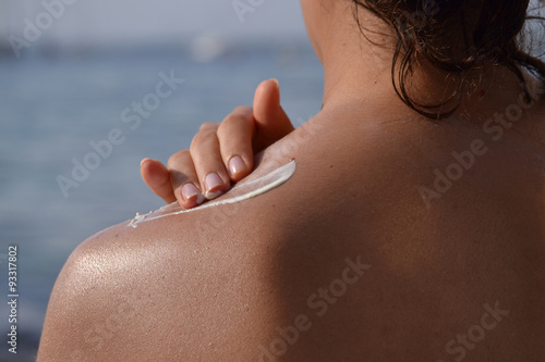 Joven mujer aplicando crema de proteccion solar en la espalda. photo