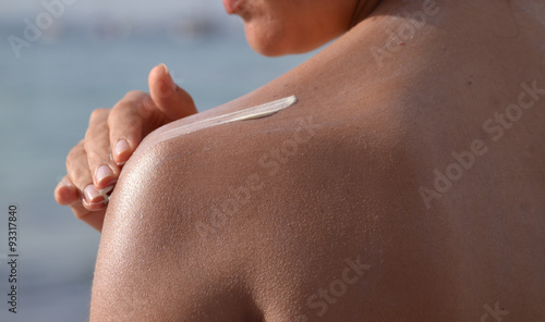 Konstfotografi Joven mujer aplicando crema de proteccion solar en la espalda.