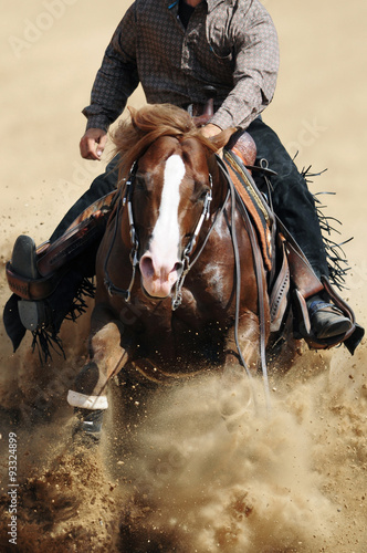 A front view of a rider and horse sliding in the dust.