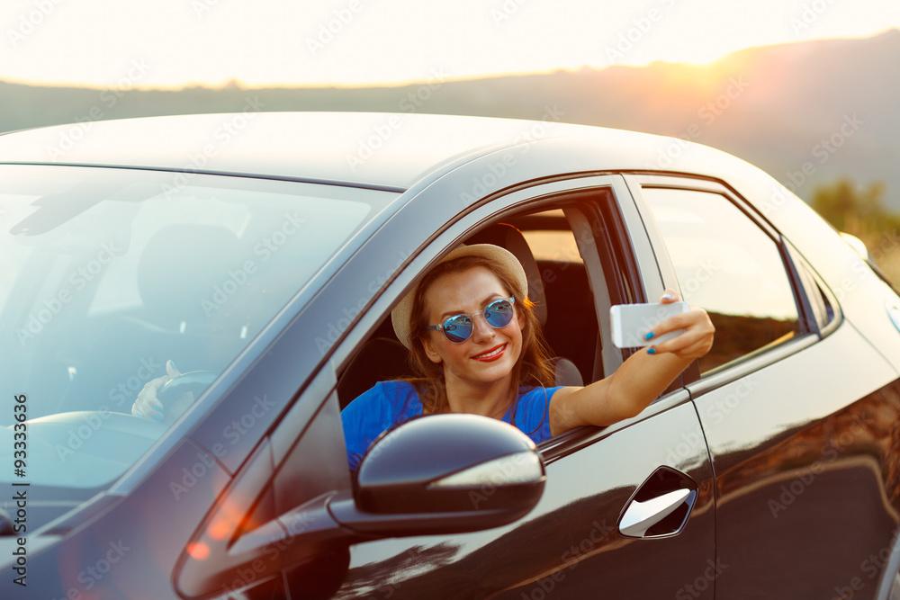 Naklejka premium Young happy woman in hat and sunglasses making self portrait sit