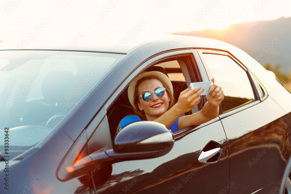 Naklejka premium Young happy woman in hat and sunglasses making self portrait sit