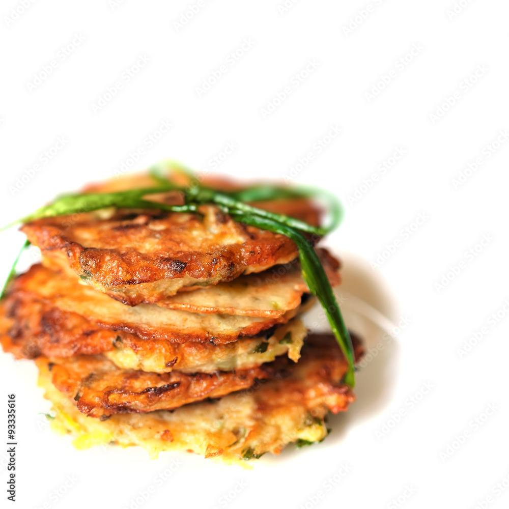 Stack of fried vegetable fritter made of zucchini, eggs, parsley, decorated with a sprig of green onions on on a white background. Selective Focus, Focus on the front of the top fritters. Stack of fried vegetable fritter made of zucchini, eggs, parsley, decorated with a sprig of green onions on on a white background. Selective Focus, Focus on the front of the top fritters.