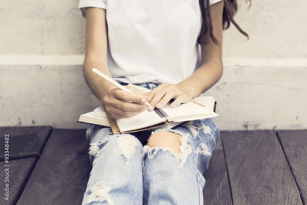 Girl making notes in the diary and sitting on a wooden floor - obrazy, fototapety, plakaty 
