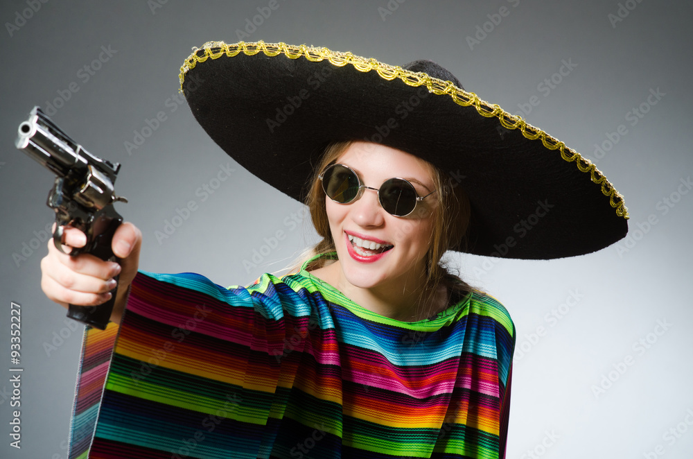 Girl in mexican vivid poncho with handgun against gray Girl in mexican vivid poncho with handgun against gray