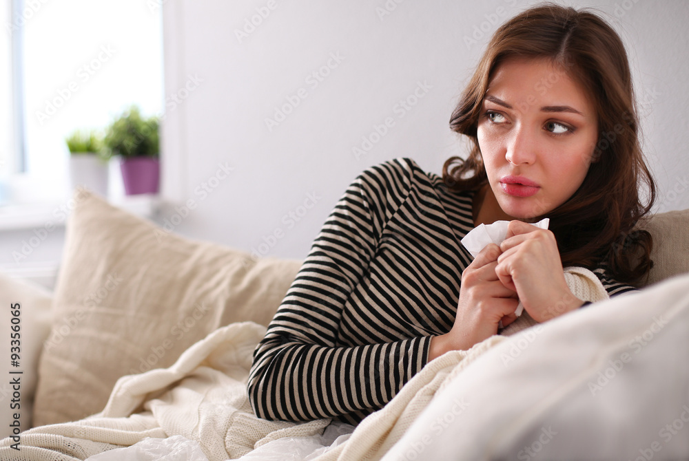 Portrait of a sick woman blowing her nose while sitting on the Portrait of a sick woman blowing her nose while sitting on the