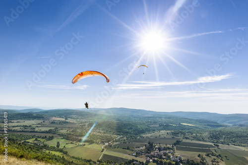 Two paragliders under the rays of a white sun