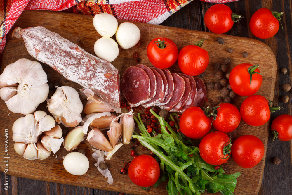 Salami with cherry tomatoes, ruccola and garlic on a cutting boa Salami with cherry tomatoes, ruccola and garlic on a cutting boa