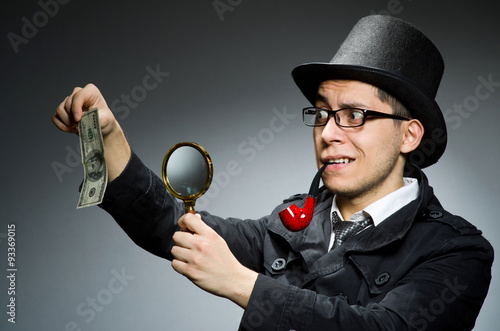 Young detective in black coat with money against gray