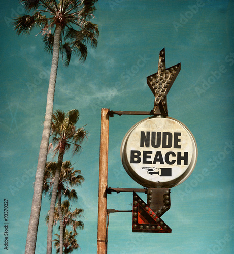 aged and worn vintage photo of nude beach sign with palm trees