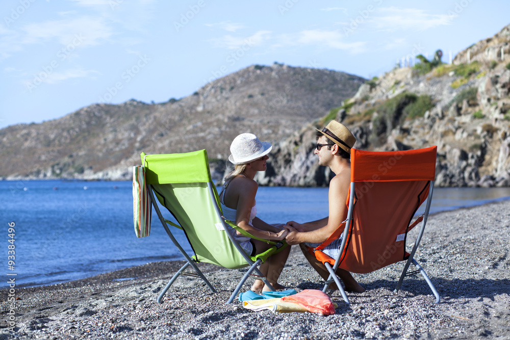 Young couple is sitting on chaise lounge at the beach Young couple is sitting on chaise lounge at the beach