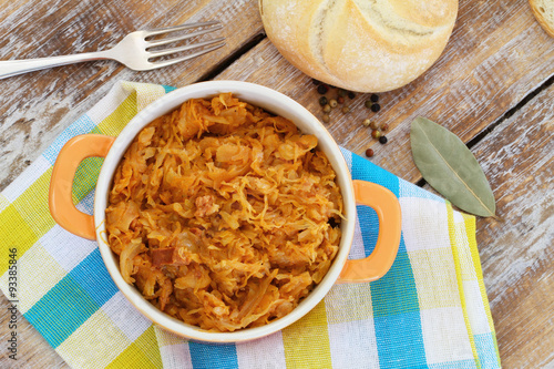 Polish bigos in saucepen on colorful kitchen cloth on rustic wooden surface
