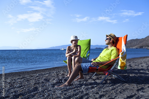 Young couple is sitting on chaise lounge at the beach