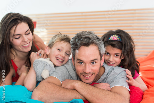 Smiling parents having fun in bed with their two children. 