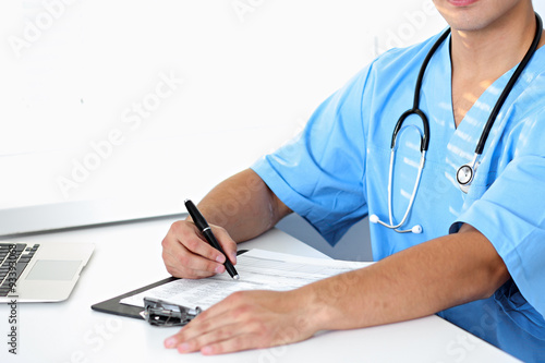 Portrait of unknown male surgeon doctor holding his stethoscope and filling up medical history