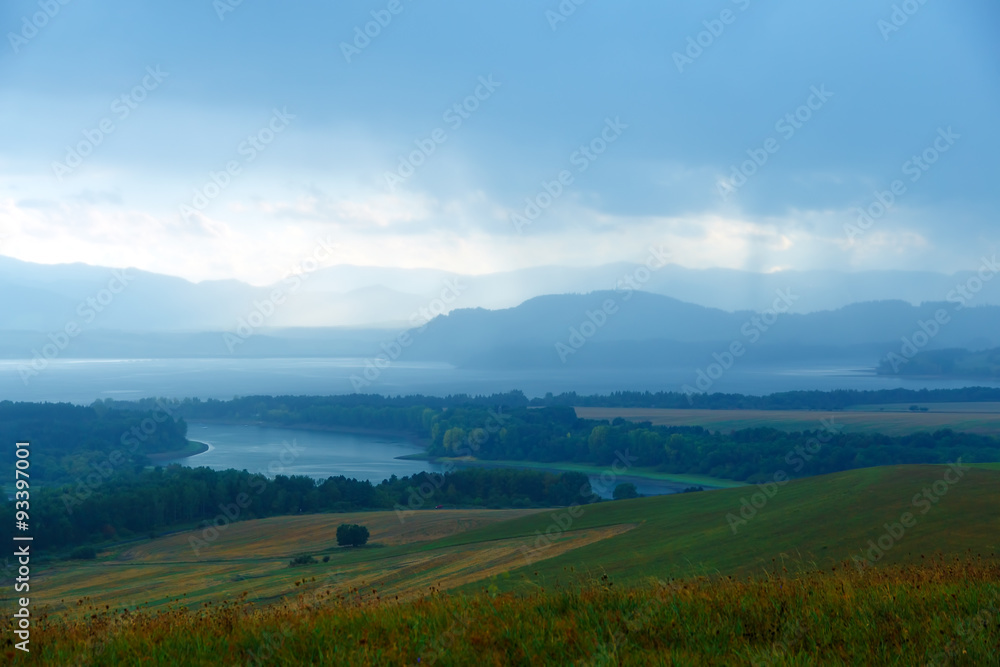 Fototapeta premium landscape with storm clouds, green and yellow meadow a lake 