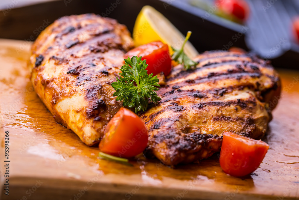 Grilled chicken breast in different variations with cherry tomatoes, green French beans, garlic, herbs, cut lemon on a wooden board or teflon pan. Traditional cuisine. Grill kitchen. 