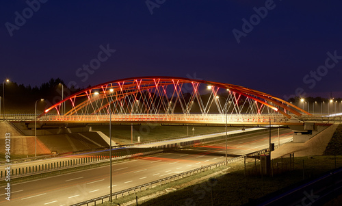 Red steel bridge over brand new highway in the night.