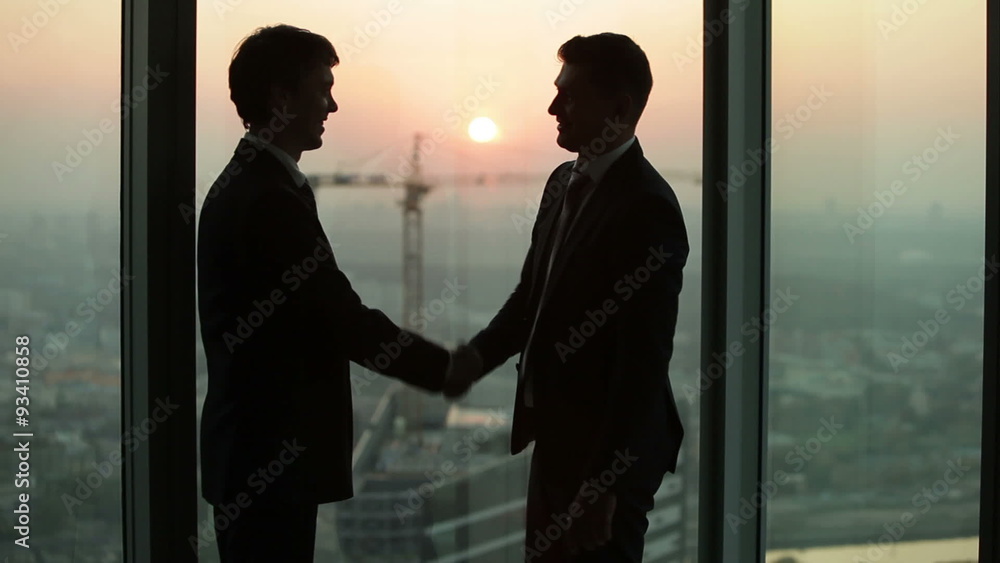 silhouette of two businessmen talking and shaking hands standing silhouette of two businessmen talking and shaking hands standing