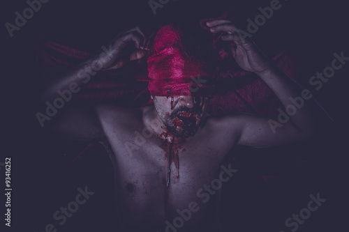 Bloody, naked man on large red cloth over his eyes