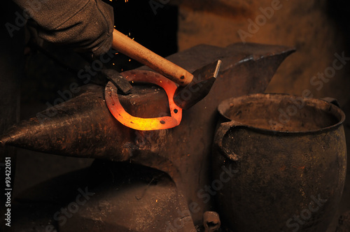 A blacksmith forging a horseshoe by a hammer