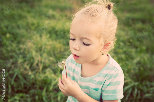 Adorable little blond girl with dandelion flower. Happy kid having fun outdoors
