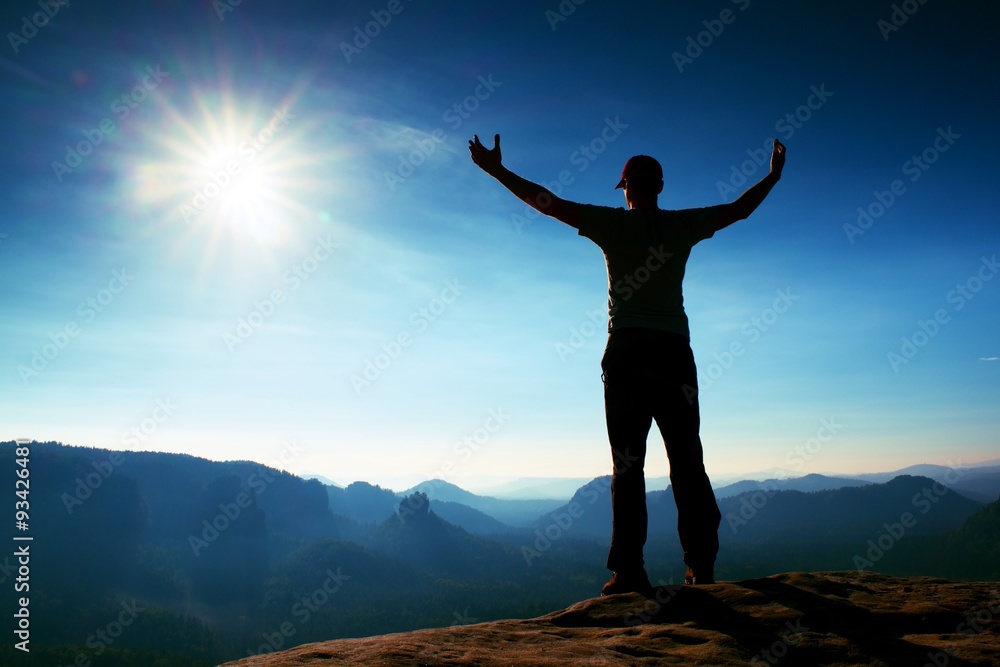 Happy man gesture in red cap of triumph with hands in the air. Funny hiker on the peak of sandstone rock in Saxony Switzerland park