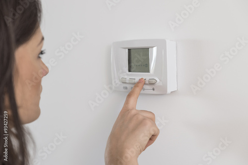 Beautiful happy woman push button digital thermostat at house