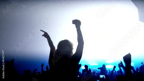 Here is  footage of people crowd partying at a concert or a night club. You can see dark silhouettes dancing, jumping and waving hands in front of stage.