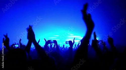 Here is  footage of people crowd partying at a concert or a night club. You can see dark silhouettes dancing, jumping and waving hands in front of stage.