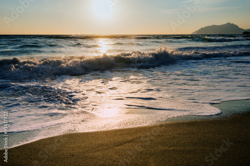 Fototapeta Naklejka Na Ścianę i Meble -  Foamy water  on sandy beach shore at sunset, Corfu, Greece. Amazing sandy beach with sea weeds and  clouds, Corfu, Greece.