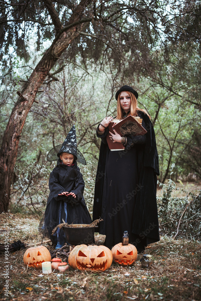 adult witch and small witch making magic in the wood. mother and daughter in halloween costumes adult witch and small witch making magic in the wood. mother and daughter in halloween costumes