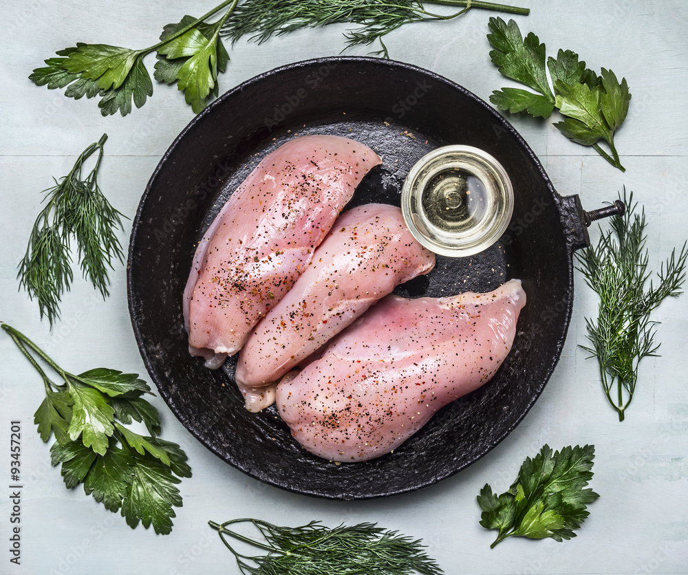 raw fresh chicken breast seasoned with oil and herbs on an old cast-iron frying pans on wooden rustic background close up top view