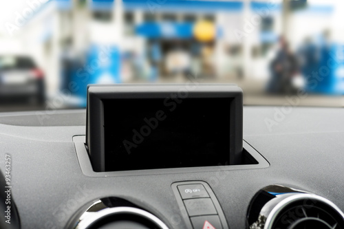 Detailed view of a display at a dashboard in a car. Under the display is the hazards button and on the sides are two car ventilation. Focus is on the black display.