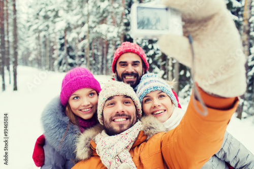 smiling friends with camera in winter forest
