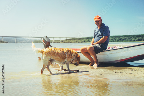 Elderly man sitting on his boat, playing catch with a dog.