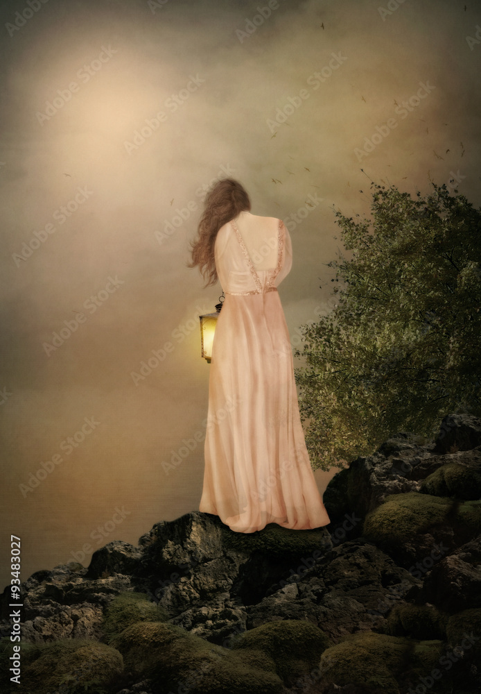 Young girl with long hair in pink dress with a lantern in her hand standing on the rock at sunset Young girl with long hair in pink dress with a lantern in her hand standing on the rock at sunset