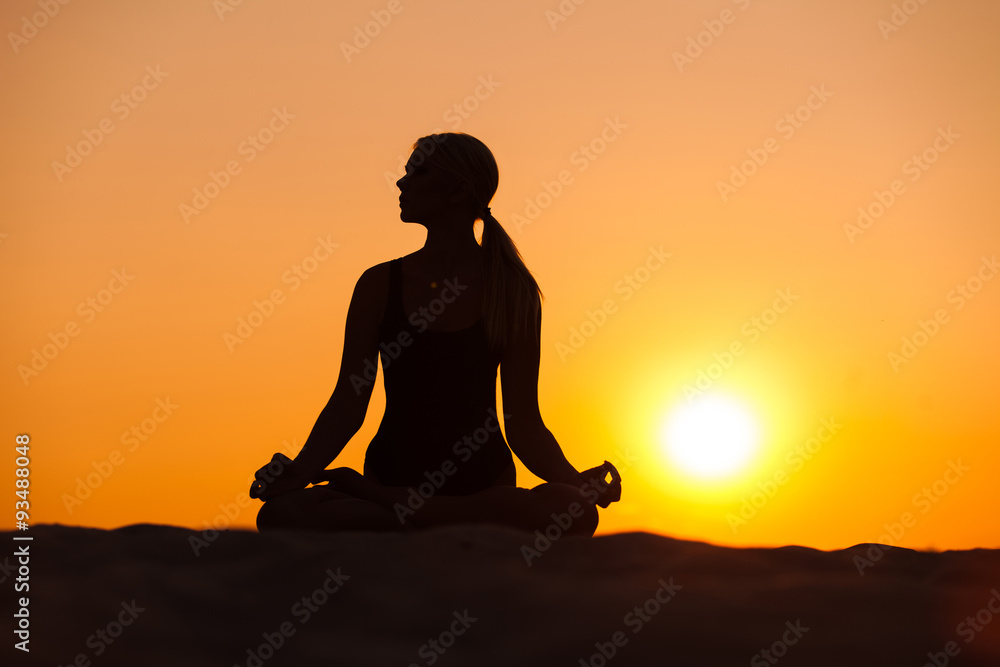 Silhouette young woman practicing yoga on sand at sunset