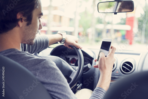 Young man driving car and using mobile phone