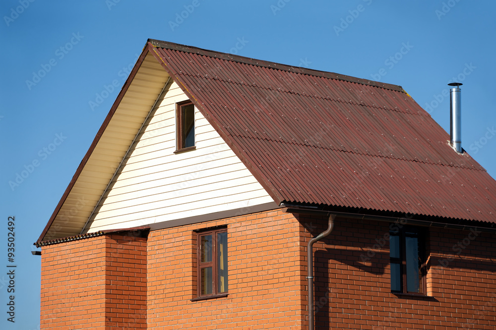 New country house of red brick, brown roof covered and siding on the front and a metal chimney New country house of red brick, brown roof covered and siding on the front and a metal chimney