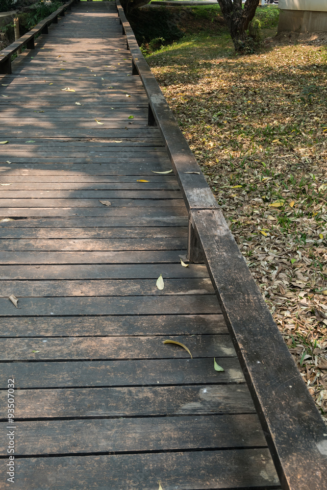 old wooden walkway with falling leaves in the morning of autumn