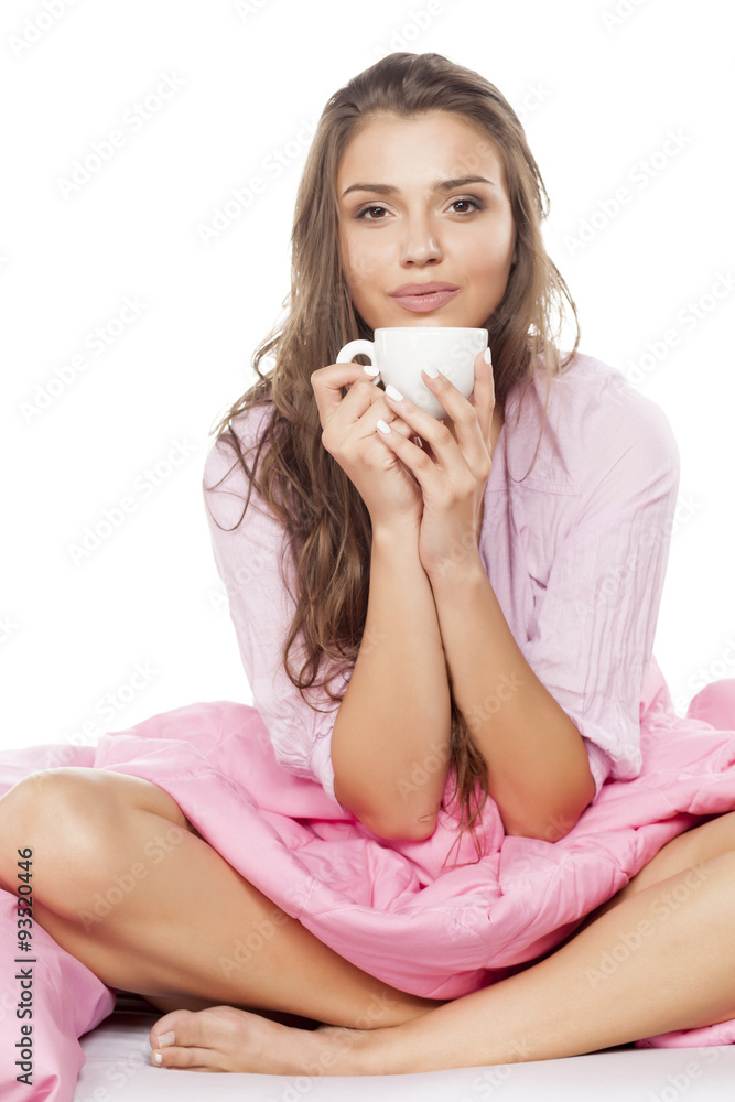 satisfied young woman sitting in bed with a cup of coffee in her hands satisfied young woman sitting in bed with a cup of coffee in her hands