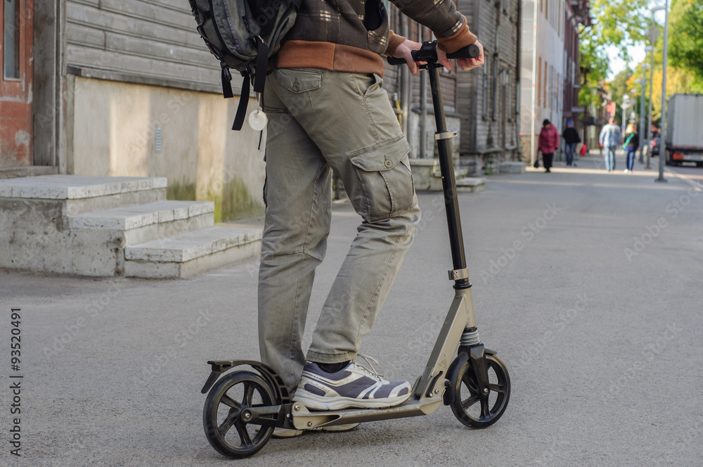 Obraz premium Young man in casual wear on kick scooter on street