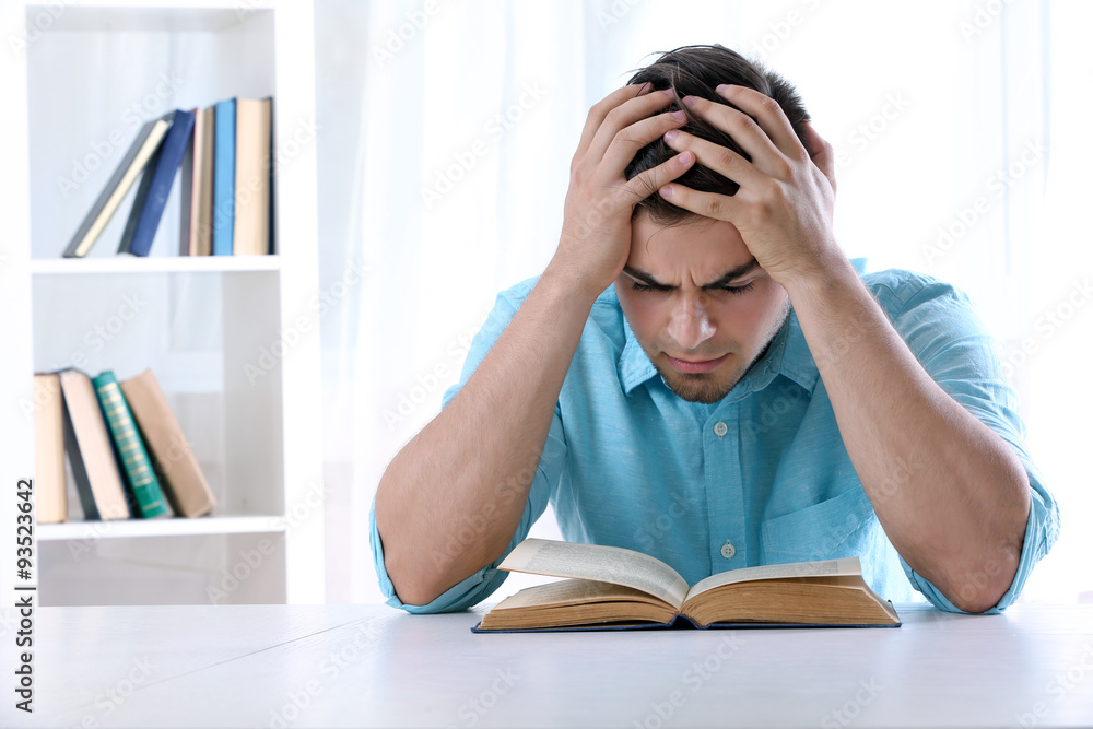 Young man reading book at table in room Young man reading book at table in room