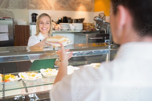 Bilde på lerret Female shop owner giving sandwich to customer