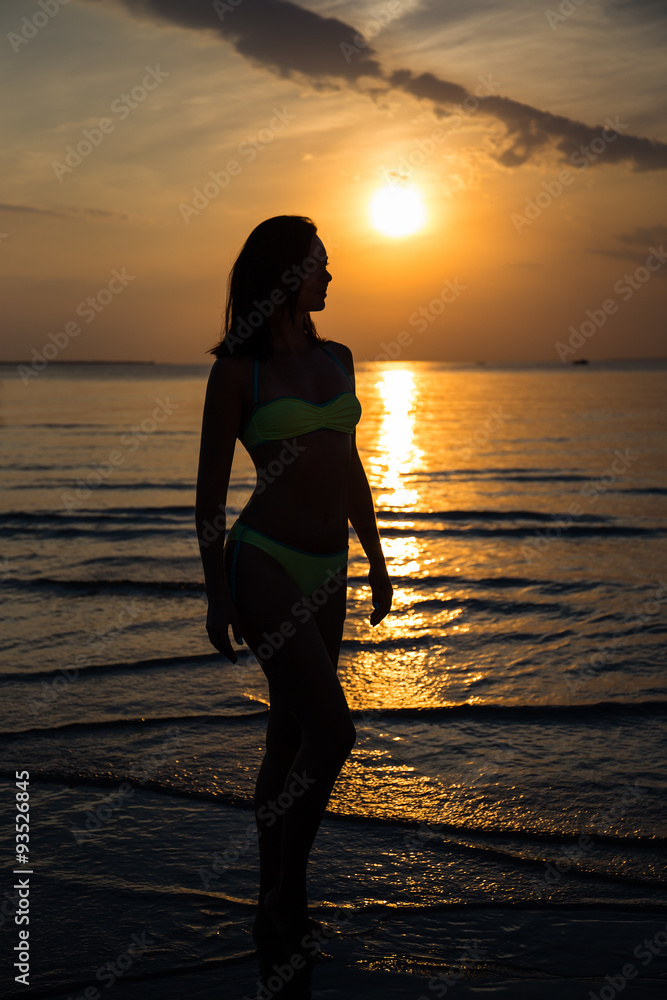 silhouette of woman in bikini walking on beach at sunset
