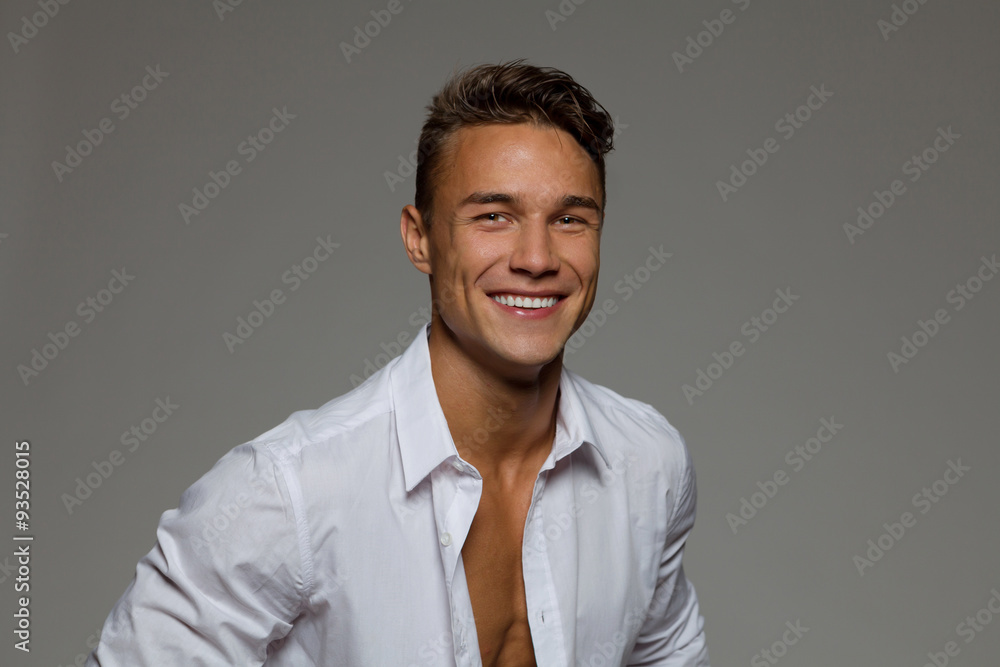 Smiling young man in white unbuttoned shirt. Studio portrait on gray background. Smiling young man in white unbuttoned shirt. Studio portrait on gray background.