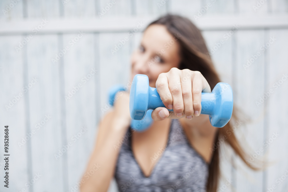 Portrait of cheerful woman in fitness wear exercising with dumbbell, outdoors Portrait of cheerful woman in fitness wear exercising with dumbbell, outdoors