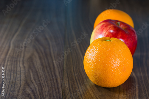 Oranges and apples in row on wooden floor.
