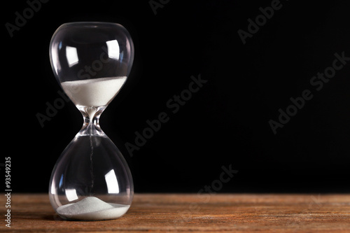 Hourglass on wooden table on black background