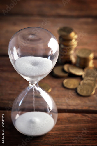 Hourglass and coins on wooden table close-up